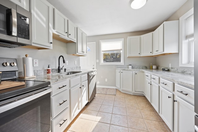 kitchen with a sink, appliances with stainless steel finishes, light stone counters, and white cabinetry