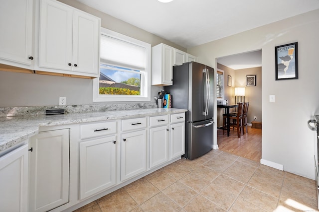 kitchen with white cabinets, light tile patterned flooring, light stone countertops, freestanding refrigerator, and baseboards