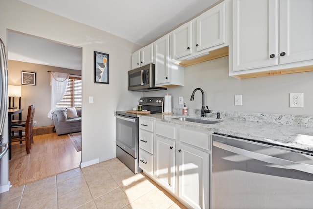 kitchen featuring appliances with stainless steel finishes, white cabinetry, a sink, light stone counters, and light tile patterned flooring
