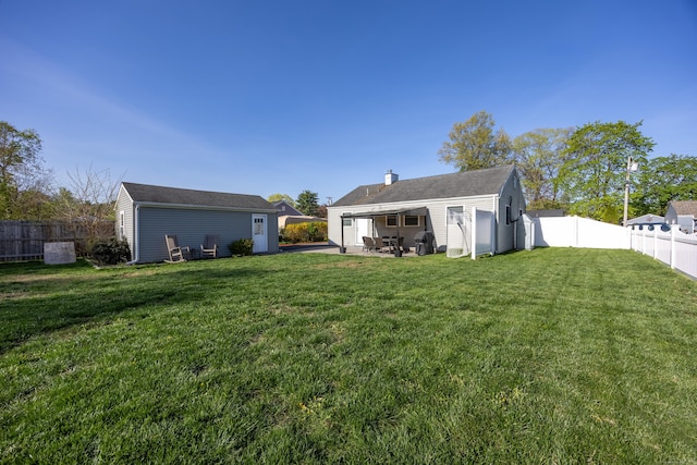 rear view of house featuring a lawn, an outdoor structure, a chimney, and a fenced backyard