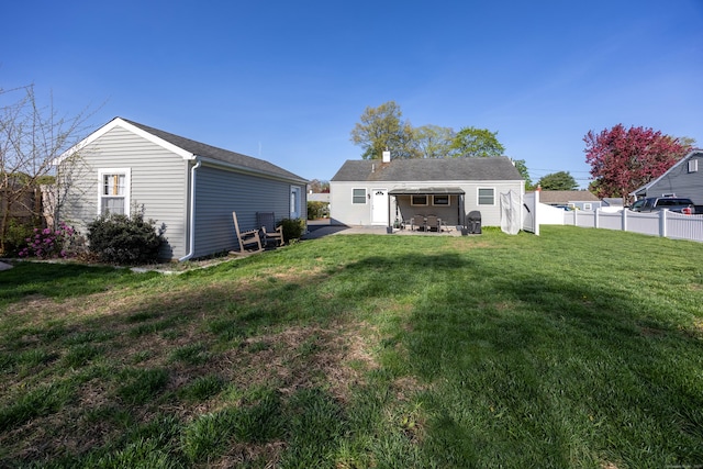 back of property featuring fence, an outbuilding, a chimney, a lawn, and a patio