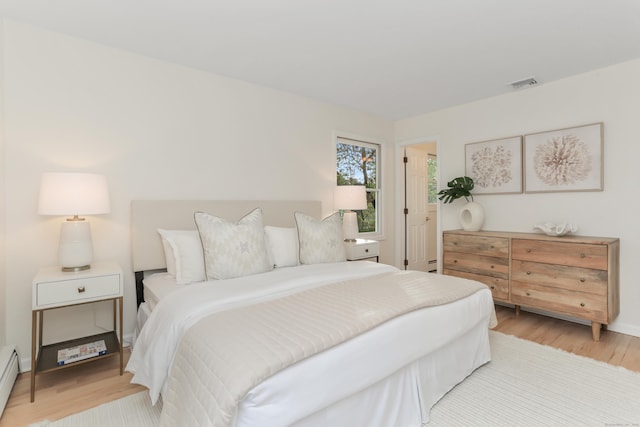 bedroom with baseboard heating, baseboards, visible vents, and light wood-style flooring