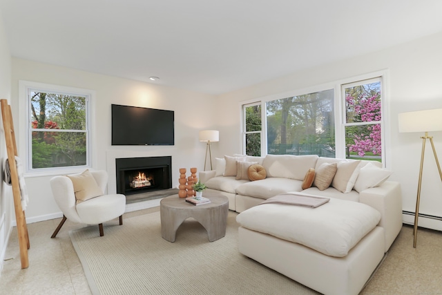 living area featuring baseboards, a baseboard heating unit, and a warm lit fireplace