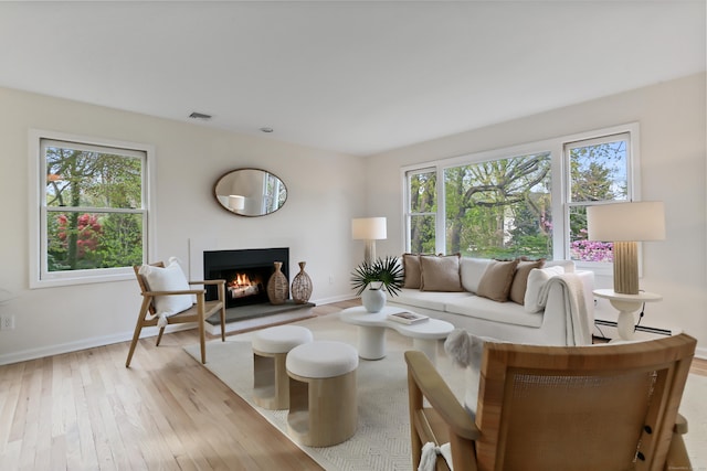 living room featuring visible vents, baseboards, a warm lit fireplace, a baseboard heating unit, and light wood finished floors