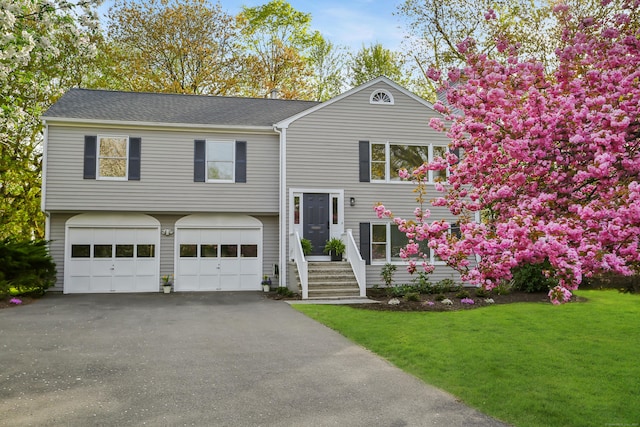 bi-level home with a garage, a shingled roof, a front yard, and aphalt driveway