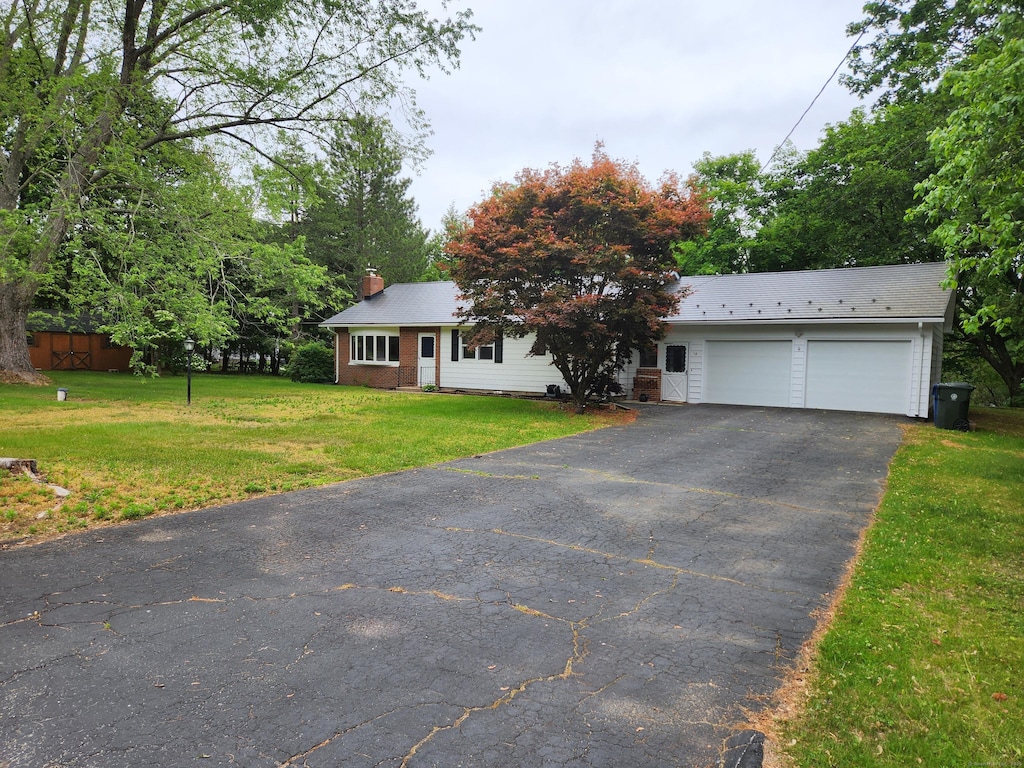 ranch-style house with a garage, a chimney, a front lawn, and aphalt driveway