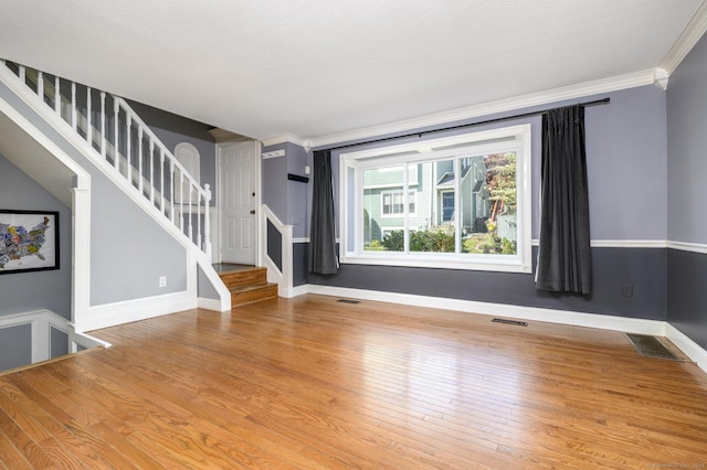 unfurnished living room featuring wood finished floors, baseboards, ornamental molding, and stairs