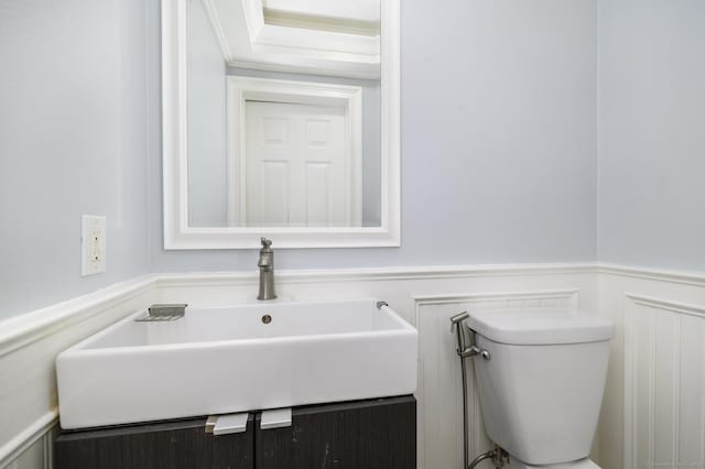 bathroom with toilet, a decorative wall, a wainscoted wall, vanity, and ornamental molding