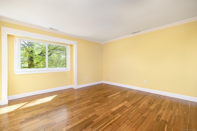 empty room featuring ornamental molding, baseboards, hardwood / wood-style floors, and visible vents