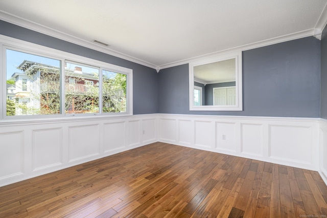 spare room with a wainscoted wall, crown molding, dark wood-type flooring, and visible vents