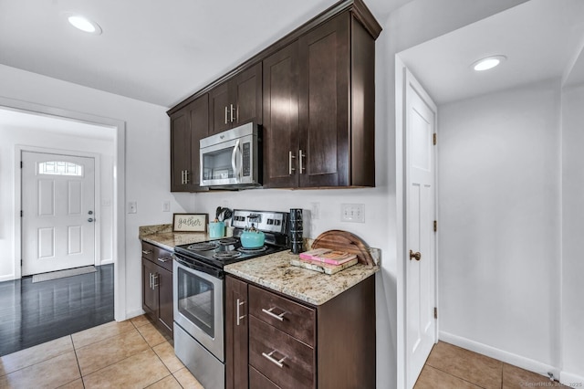 kitchen with dark brown cabinetry, appliances with stainless steel finishes, light stone countertops, baseboards, and light tile patterned floors