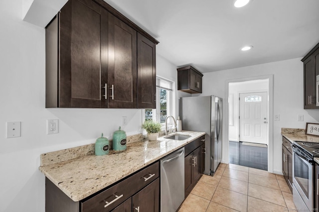 kitchen featuring dark brown cabinets, a sink, light stone counters, stainless steel appliances, and light tile patterned flooring