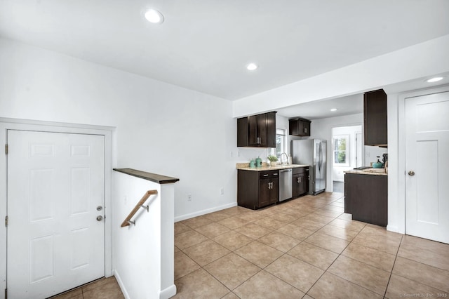 kitchen with dark brown cabinetry, light countertops, light tile patterned floors, a sink, and stainless steel appliances
