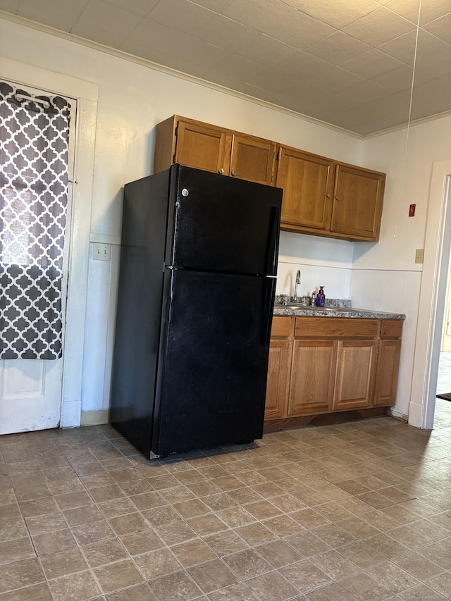 kitchen with stone finish floor, brown cabinets, crown molding, a wainscoted wall, and freestanding refrigerator