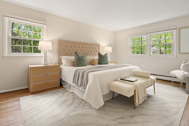 bedroom with a baseboard heating unit, light wood-style flooring, and baseboards