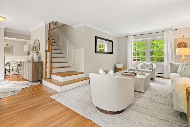 living room with ornamental molding, light wood finished floors, stairs, baseboard heating, and wainscoting