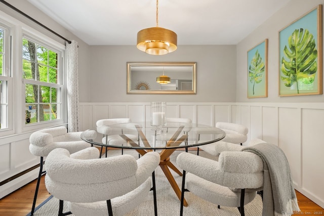 dining space featuring baseboard heating, a decorative wall, wood finished floors, and a wainscoted wall