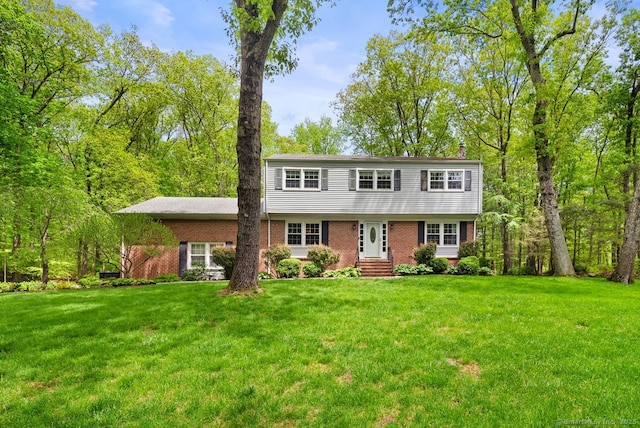 colonial home with brick siding, a front yard, entry steps, and a chimney