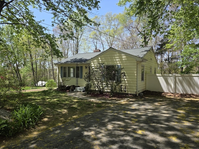 view of side of property featuring fence, a chimney, and a shingled roof