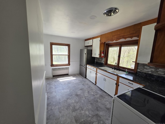 kitchen with dark countertops, a sink, stove, radiator, and decorative backsplash