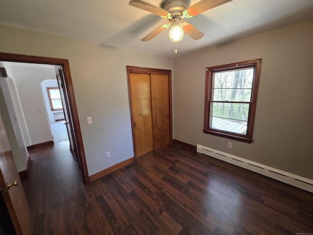 unfurnished bedroom featuring baseboards, multiple windows, a baseboard heating unit, and dark wood-style flooring