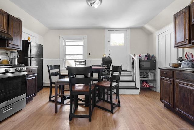 dining space with vaulted ceiling, wainscoting, and light wood finished floors