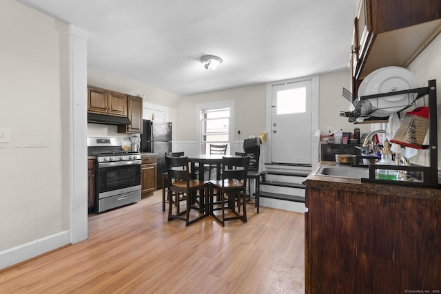kitchen with a sink, gas range, baseboards, light wood-type flooring, and under cabinet range hood