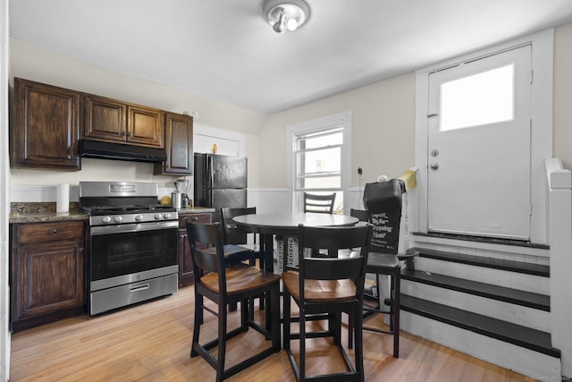 kitchen featuring light wood-style flooring, under cabinet range hood, dark brown cabinetry, and stainless steel gas range
