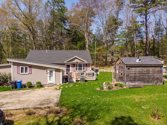 back of house with a lawn, a deck, an outdoor structure, and roof with shingles