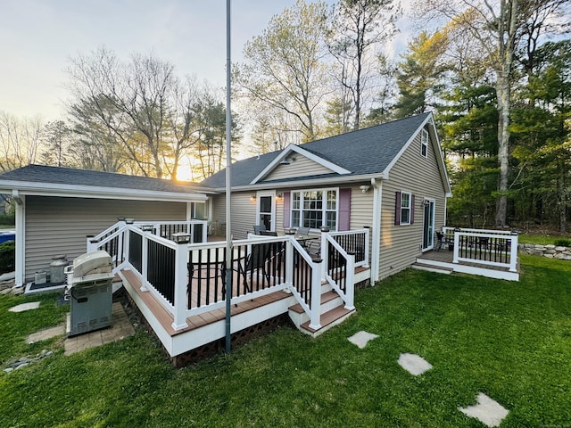 rear view of house with a yard, a deck, and a shingled roof