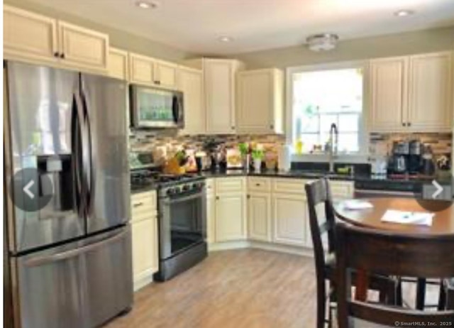 kitchen with decorative backsplash, dark countertops, light wood-type flooring, a sink, and stainless steel appliances