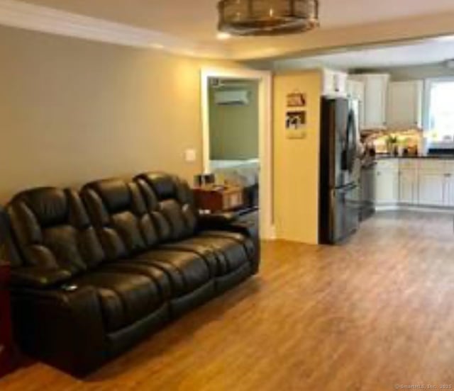 living area with ornamental molding, a wall mounted AC, and wood finished floors