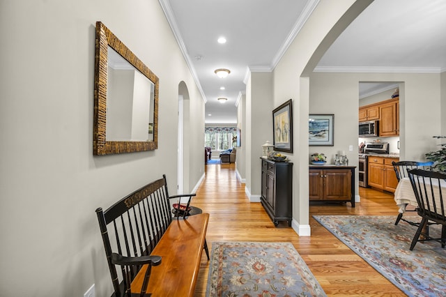 hallway featuring arched walkways, baseboards, ornamental molding, and light wood finished floors