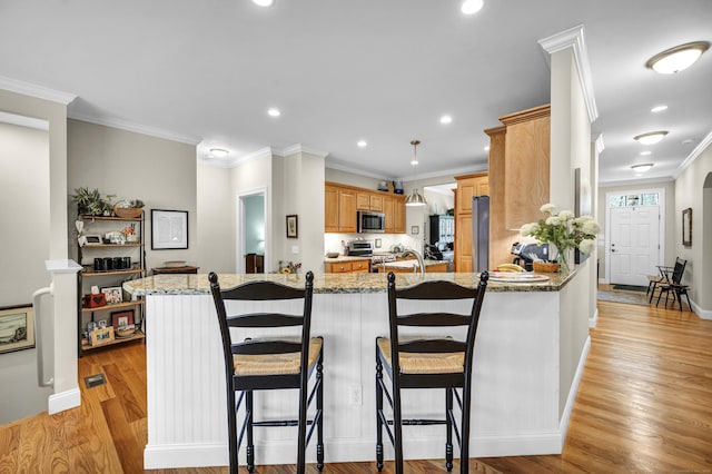 kitchen with a peninsula, a breakfast bar, light stone counters, light wood finished floors, and stainless steel appliances