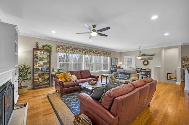 living area with a ceiling fan, crown molding, a fireplace with raised hearth, light wood finished floors, and recessed lighting