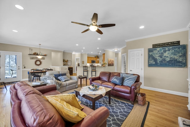 living room featuring light wood-style floors, a ceiling fan, baseboards, and ornamental molding