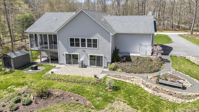 rear view of property featuring a shingled roof, a sunroom, a patio area, and a shed