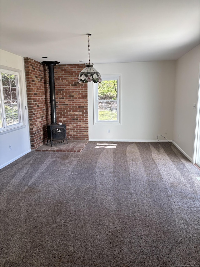 unfurnished living room with carpet floors, baseboards, and a wood stove