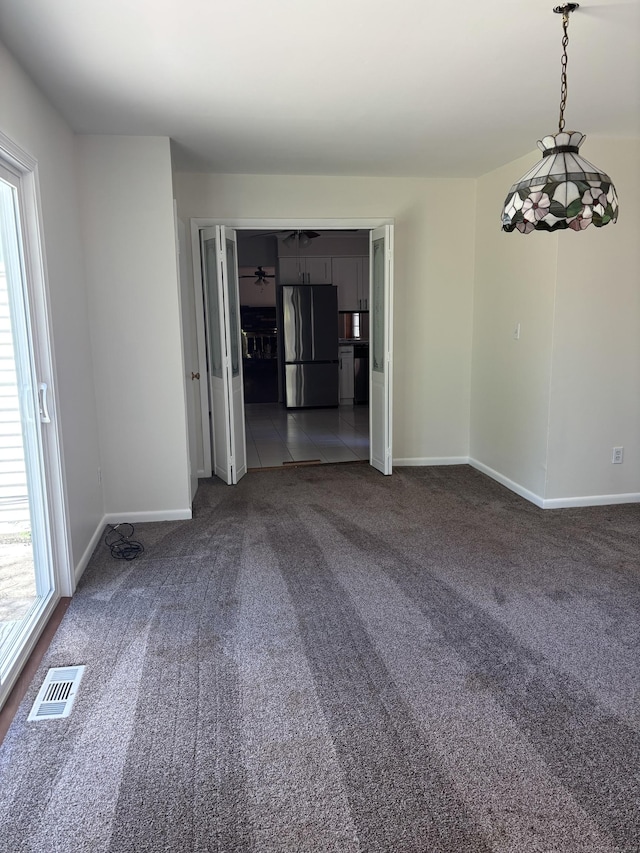 spare room featuring a wealth of natural light, dark carpet, and visible vents