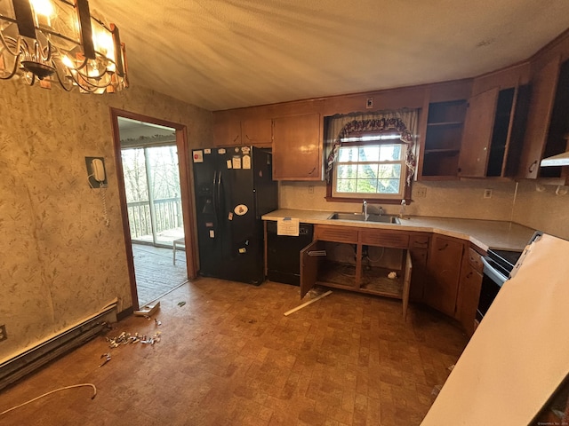 kitchen with wall chimney range hood, black appliances, light countertops, a sink, and a notable chandelier