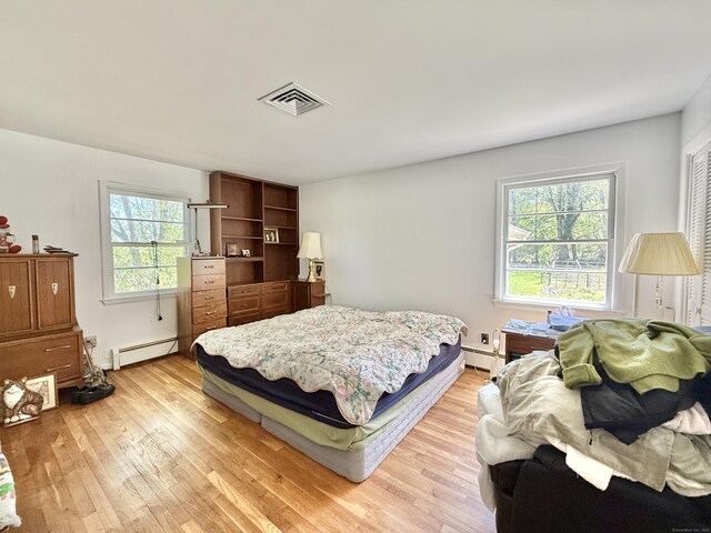 bedroom featuring visible vents, baseboard heating, and light wood-style flooring