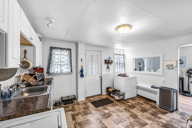 interior space featuring dark countertops, a sink, radiator heating unit, white cabinetry, and washer / dryer