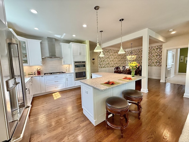kitchen featuring wall chimney range hood, stainless steel appliances, white cabinets, and a kitchen island
