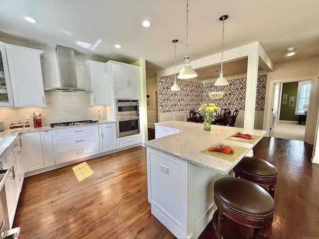 kitchen featuring white cabinetry, a kitchen bar, wall chimney range hood, and stainless steel appliances