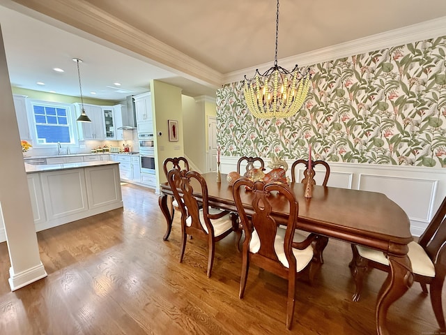 dining space featuring crown molding, wood finished floors, a wainscoted wall, an inviting chandelier, and recessed lighting