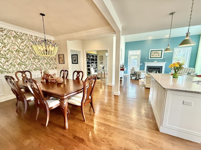 dining room featuring ornamental molding, a fireplace, a wainscoted wall, a chandelier, and light wood finished floors