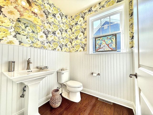 half bathroom with visible vents, wainscoting, wood finished floors, toilet, and wallpapered walls