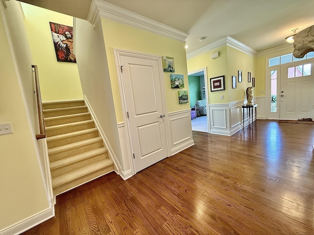 foyer entrance with crown molding, a wainscoted wall, dark wood finished floors, and stairs