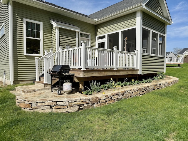 rear view of property featuring a yard, a deck, a sunroom, and roof with shingles