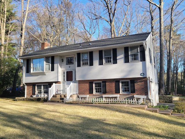 raised ranch featuring a chimney, a front lawn, and brick siding